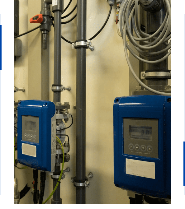 Two blue industrial devices mounted on a wall with piping and cables.