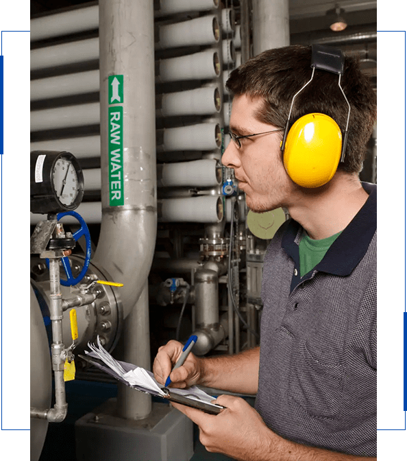 Technician inspecting industrial machinery with safety headphones and clipboard.